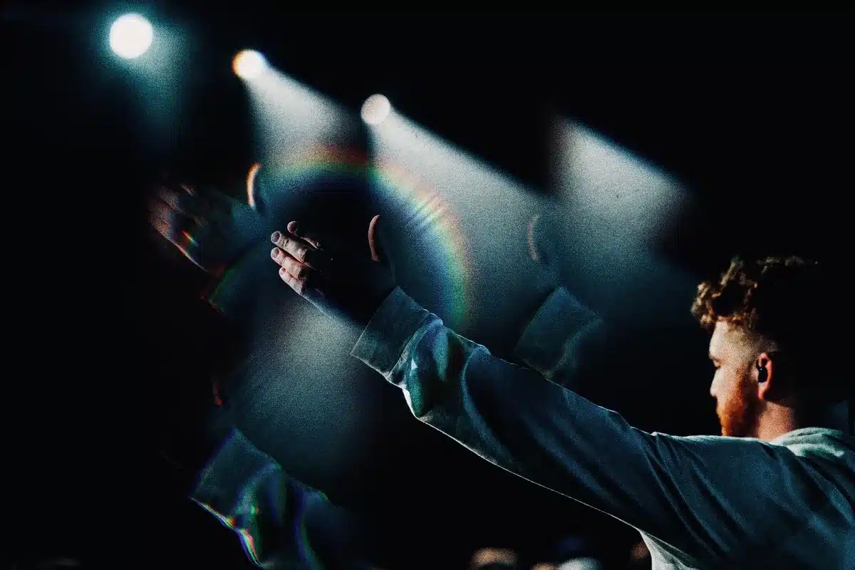 A performer stands on stage under warm lighting in a large modern arena, preparing to perform live.