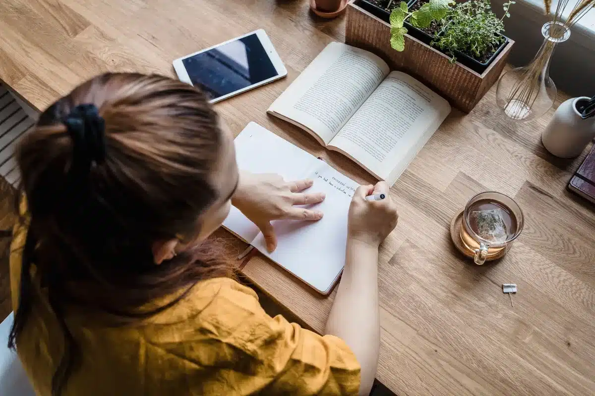 Femme écrivant dans un journal, entourée de livres et de documents, symbolisant l'acte d'écrire pour guérir