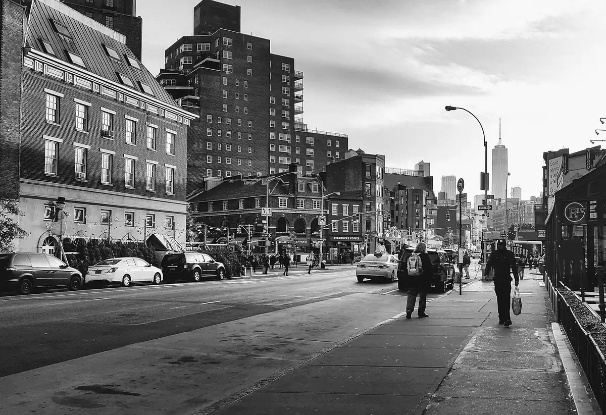 Person walking on a sunny Manhattan sidewalk wearing denim and a tailored coat