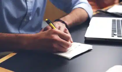Hands typing on a laptop in a bright home office with a phone and notebook on the desk