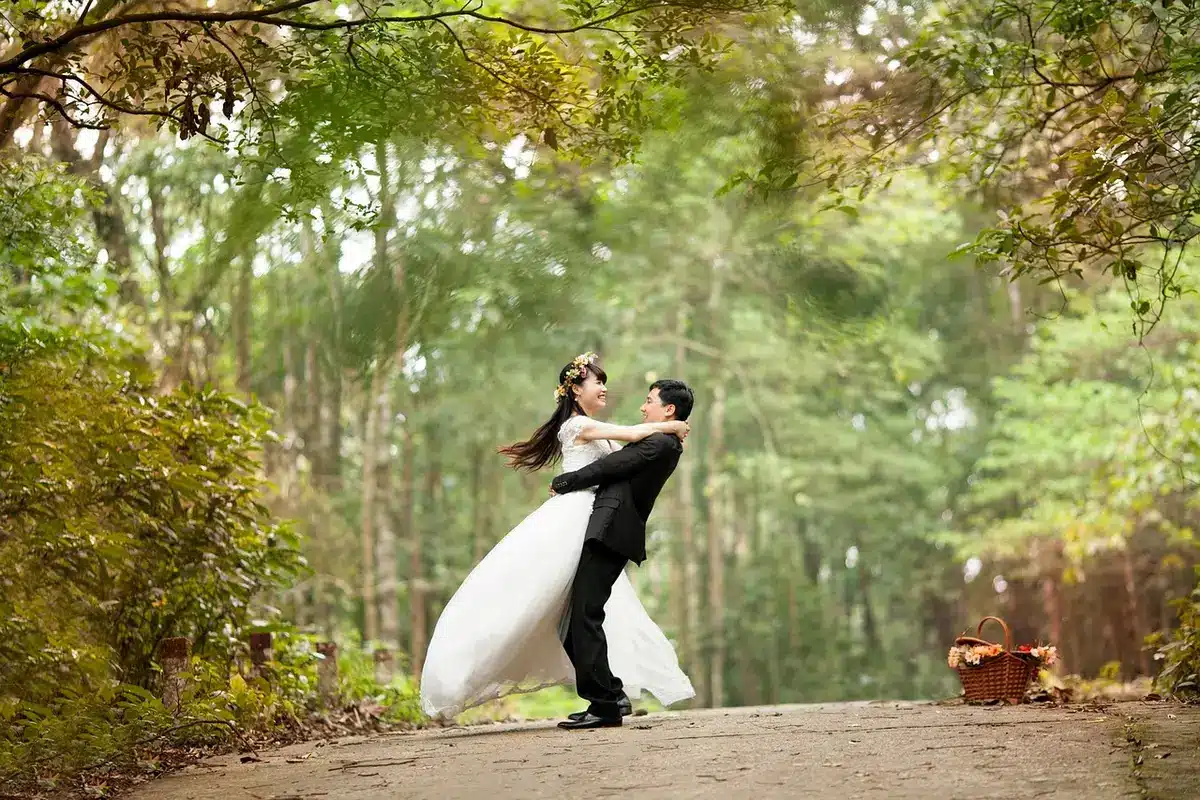 Hands holding wedding bands beside a bouquet on a sunlit outdoor table